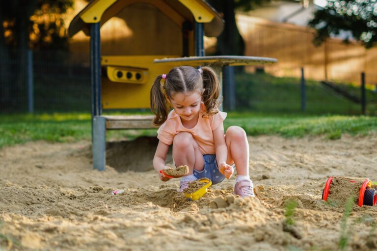 cute toddler girl playing in sand on outdoor playground